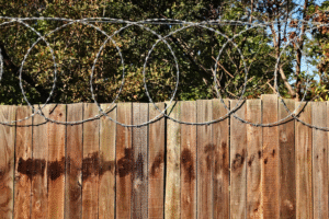 A deteriorating wooden fence with barbed wire and exposed nails in a yard
